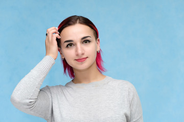 Portrait of the chest of a pretty girl with red hair on a blue background in a gray jacket. Standing in the studio right in front of the camera with emotions, talking, showing hands, smiling