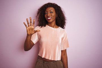 Young african american woman wearing t-shirt standing over isolated pink background showing and pointing up with fingers number five while smiling confident and happy.