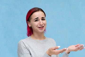 Portrait of the chest of a pretty girl with red hair on a blue background in a gray jacket. Standing in the studio right in front of the camera with emotions, talking, showing hands, smiling