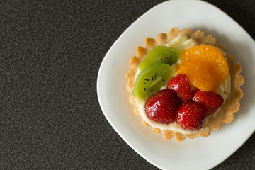 Cake with cream, raspberries, kiwi and orange on a black background. Pastry with fruits on top. Sweet dessert. Copy space.