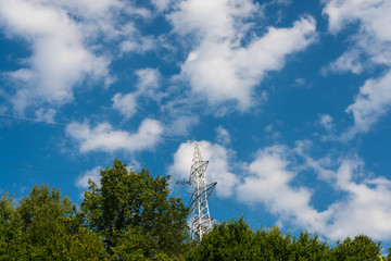 Electricity pylon , green trees outdoor against blue sky with white clouds.