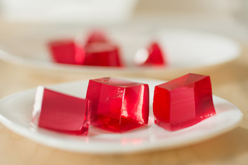 Red jelly cubes on white plate background. Berry sweet pieces of jelly. Homemade red cherry gelatin dessert.