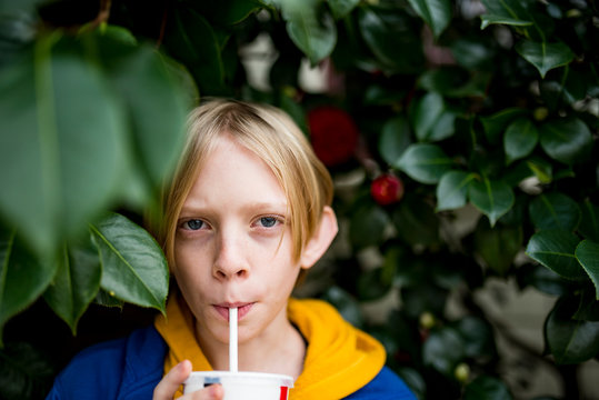 Teenage boy drinking from straw surrounded by green foliage