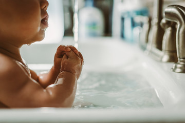 Baby getting sink bath with water drops and rubberband wrists
