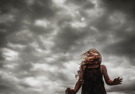Little girl w/ curly hair delighting in the wind with dark clouds sky