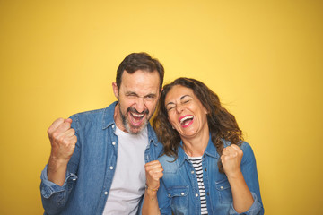 Beautiful middle age couple together wearing denim shirt over isolated yellow background very happy...