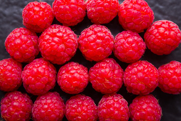 Raspberries on a dark background. Red raspberry on a black plate. Red berries on wooden boards. Top view. Copy space