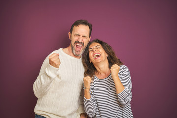 Beautiful middle age couple wearing winter sweater over isolated purple background very happy and excited doing winner gesture with arms raised, smiling and screaming for success. Celebration concept.