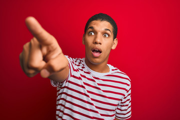 Fototapeta premium Young handsome arab man wearing striped t-shirt over isolated red background Pointing with finger surprised ahead, open mouth amazed expression, something on the front