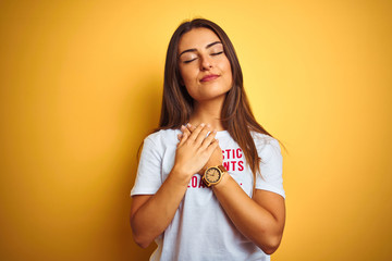 Obraz premium Beautiful woman wearing fanny t-shirt with irony comments over isolated yellow background smiling with hands on chest with closed eyes and grateful gesture on face. Health concept.