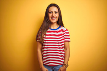 Young beautiful woman wearing striped t-shirt standing over isolated yellow background with a happy and cool smile on face. Lucky person.