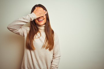 Young beautiful woman wearing winter turtleneck sweater over isolated white background smiling and laughing with hand on face covering eyes for surprise. Blind concept.