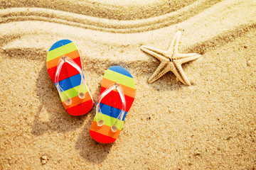 Fototapeta na wymiar Vacation background with bright flip flops and starfish on sand, top view
