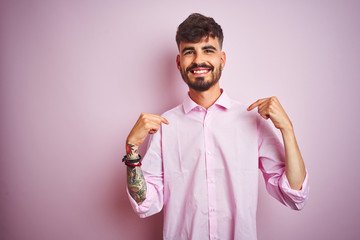 Young man with tattoo wearing shirt standing over isolated pink background looking confident with smile on face, pointing oneself with fingers proud and happy.