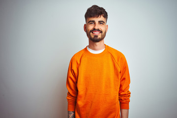 Young man with tattoo wearing orange sweater standing over isolated white background with a happy...
