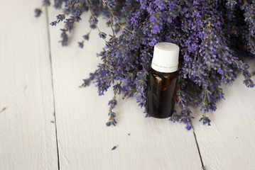 Obraz na płótnie Canvas A dark glass jar of lavender essential aromatic oil stands in a purple bouquet of flowers.