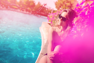 Portrait of beautiful woman wearing sunglasses by the pool, getting a nice tan