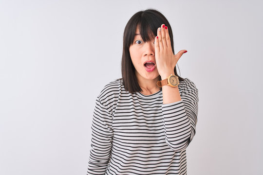 Young beautiful chinese woman wearing black striped t-shirt over isolated white background covering one eye with hand, confident smile on face and surprise emotion.