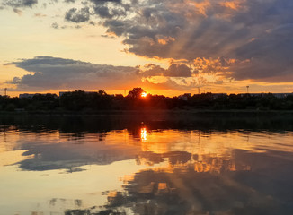 Naklejka premium Wonderful sunset over the city horizon with reflection on the calm lake water in a silent summer evening