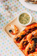 Top view of Thai grilled prawns (shrimps) in the shell and without shell in wooden plate served with Thai style spicy sauce.
