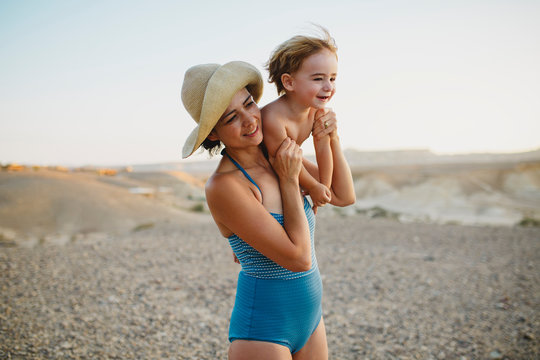 A mother wearing a hat holding her son up her shoulder  in the desert