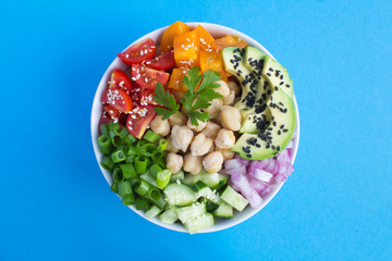 Vegan poke bowl with chickpea  and vegetables in the white bowl in the center of the blue ...