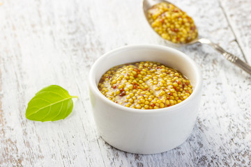 French grain mustard in a bowl on white wooden table.