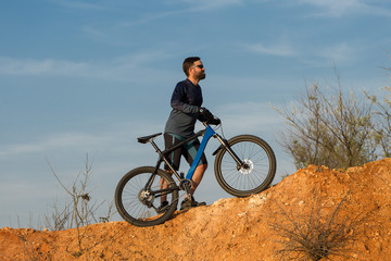 Cyclist in shorts and jersey on a modern carbon hardtail bike with an air suspension fork rides off-road on the orange-red hills at sunset evening in summer	