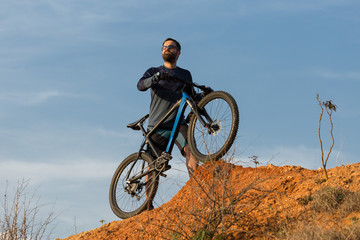 Cyclist in shorts and jersey on a modern carbon hardtail bike with an air suspension fork rides off-road on the orange-red hills at sunset evening in summer	