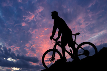 Obraz premium Cyclist in shorts and jersey on a modern carbon hardtail bike with an air suspension fork rides off-road on the orange-red hills at sunset evening in summer 