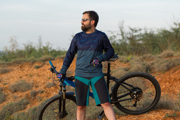 Fototapeta premium Cyclist in shorts and jersey on a modern carbon hardtail bike with an air suspension fork rides off-road on the orange-red hills at sunset evening in summer 