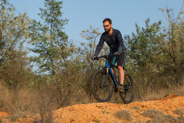 Fototapeta premium Cyclist in shorts and jersey on a modern carbon hardtail bike with an air suspension fork rides off-road on the orange-red hills at sunset evening in summer 