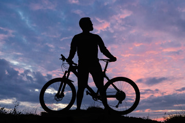 Obraz premium Cyclist in shorts and jersey on a modern carbon hardtail bike with an air suspension fork rides off-road on the orange-red hills at sunset evening in summer 