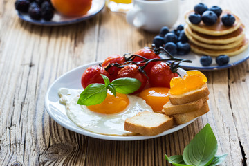  Fried eggs with cherry tomatoes, pancakes, fresh summer fruits, berries, coffee and juice