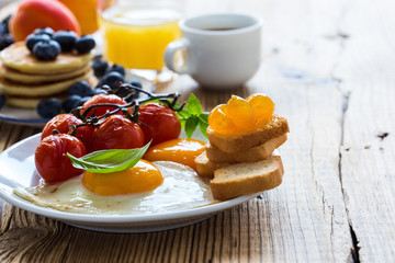  Fried eggs with cherry tomatoes, pancakes, fresh summer fruits, berries, coffee and juice