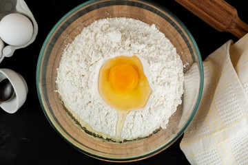 Wheat flour with egg in glass bowl on wooden cutting board, top view