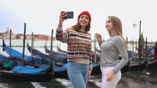 Two young women on the waterfront with boats talking and take selfie