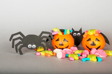 Happy Halloween Trick or Treat jack-o-lantern buckets, bat, spider and pile of colorful sweets candy on gray background. Plastic pumpkins  to collect candy.