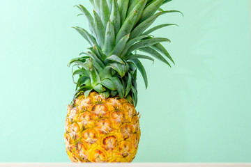 Close up of pineapple on white wooden table over neo mint background. Tropical summer vacation and beach party.