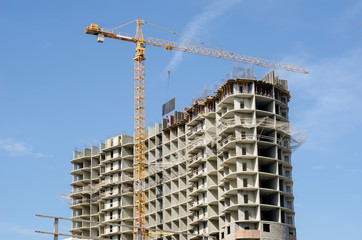 Yellow high-rise crane and house under construction against the blue sky.