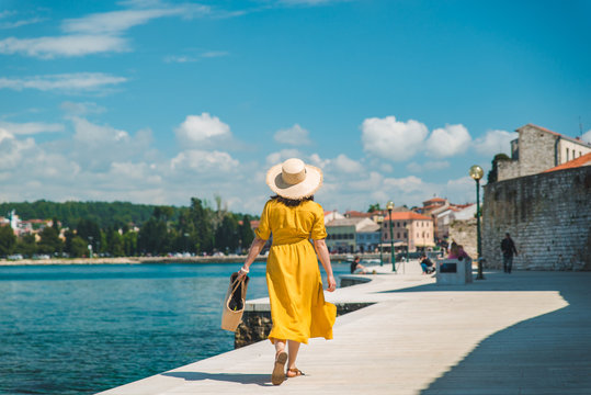 woman walking by sea quay in summer day in yellow sundress