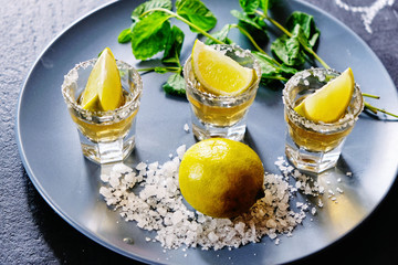 Gold tequila shot with lime and sea salt on grey plate.
