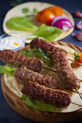 Lamb kebabs on serving board with pita bread, vegetables and yogurt sauce