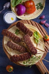 Lamb kebabs on serving board with pita bread, vegetables and yogurt sauce. View from above, top studio shot