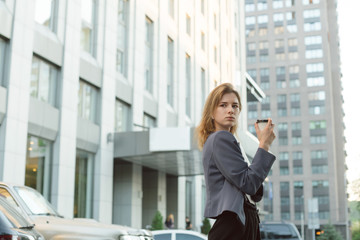 Fototapeta premium Prosperous female entrepreneur in formal wear looking back seriously while holding coffee cup walking on street, busy businesswoman satisfied with successful news after work in the business center.
