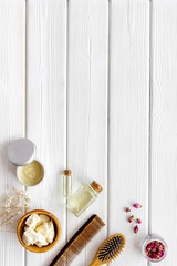 Bottle with jojoba, argan or coconut oil, styling, comb for hair style on white wooden background top view mock up