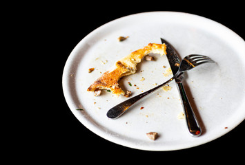There is a plate on the table and a small piece of bitten pizza in the plate.