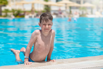 Smiling European boy on side of swimming pool at resort on summer.