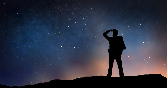 travel, tourism, hike and people concept - silhouette of traveler standing on edge and looking far away over starry night sky or space background