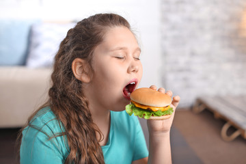 Overweight girl eating burger indoors